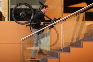 A man carries the Ampler Curt ebike over his shoulder up a flight of stairs.