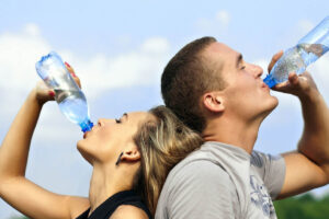 A woman and a man each drinking a bottle of water